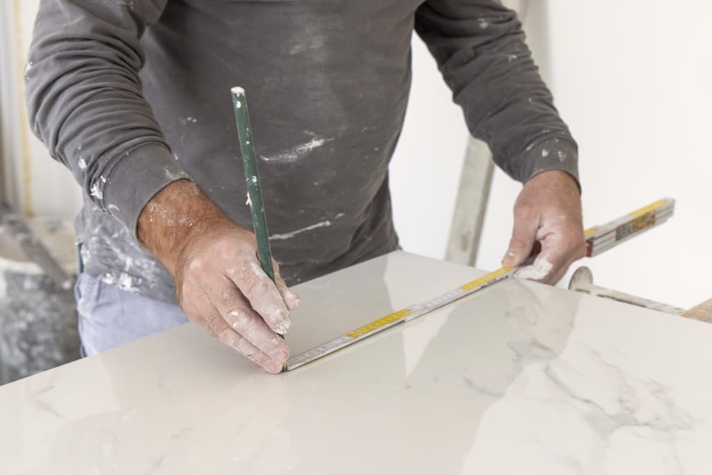 Fliese wird mit Zollstock und Stift angerissen