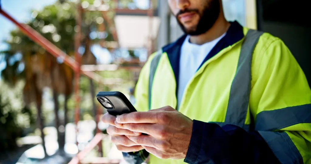 Tradesperson in a high-vis jacket using an iPhone on site